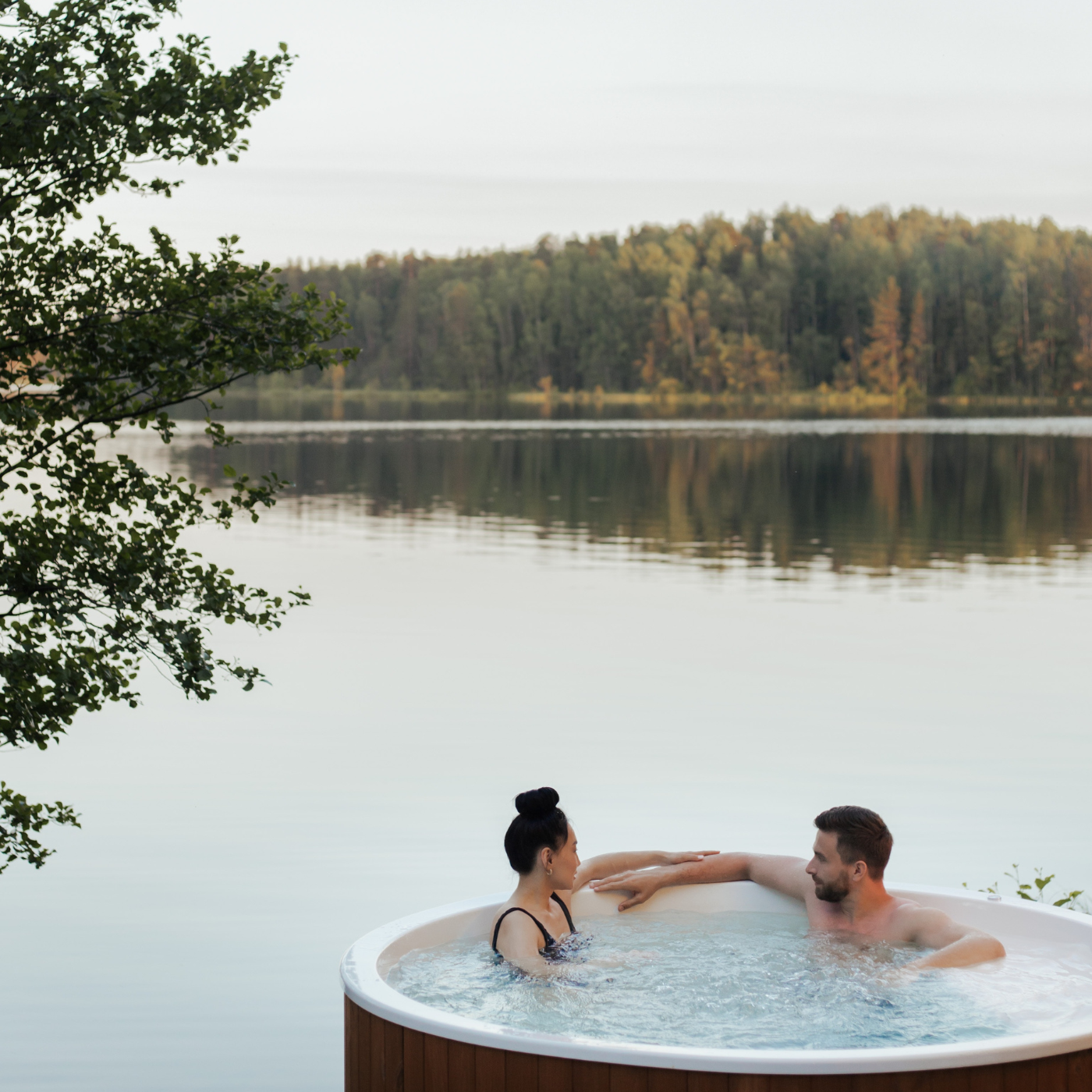 Mann und Frau sitzen in einem Whirlpool an einem See