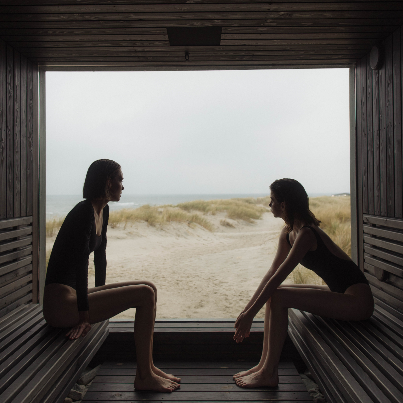 Zwei Frauen sitzen in einer Sauna und blicken auf den Strand